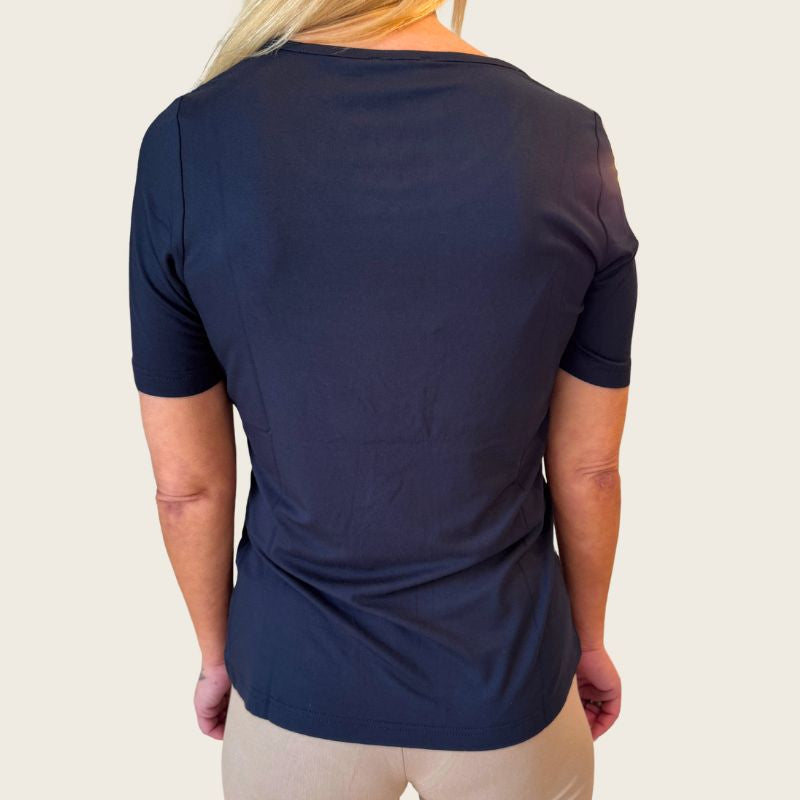En person med langt blondt hår ses bagfra iført en marinefarvet E Avantgarde T-shirt og beige bukser. Den ensfarvede, lyse baggrund fremhæver det OEKO-TEX-certificerede tøj.