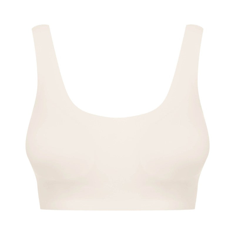 Hendersons sømløse, lysbeige bralette har en bred rund halsudskæring og tykke stropper, der giver komfort og støtte. Den er fremstillet af glat, elastisk stof uden synlige sømme eller udsmykninger og vises på en almindelig hvid baggrund. Der medfølger ingen bøjle.