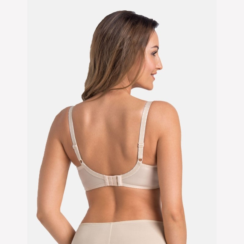 En kvinde med lysebrunt hår, der er drejet lidt til venstre, står model til en beige Teyli Komfort BH med justerbare stropper og hægtelukning bagpå. Hun har matchende beige undertøj på mod en almindelig hvid baggrund og vender væk fra kameraet.