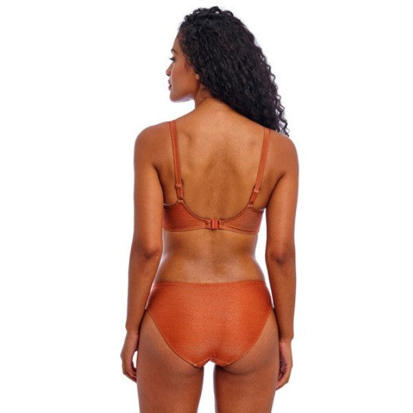 En kvinde med langt krøllet hår vender ryggen væk og er iført en bronzefarvet tekstureret bikini fra Freya. Den justerbare top har en spænde bagpå, og trusserne med mellemhøj talje giver moderat dækning. Hun står mod en almindelig hvid baggrund.