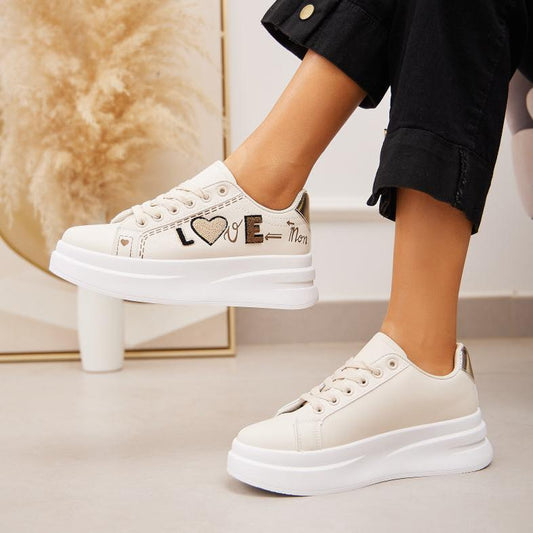 Den hvide sneakers har fine guld detaljer. Detaljerne ses bagpå skoen, med snørebåndene.