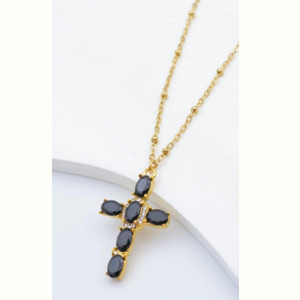 Guldfarvet halskæde med et korsformet vedhæng dekoreret med sorte og klare sten.