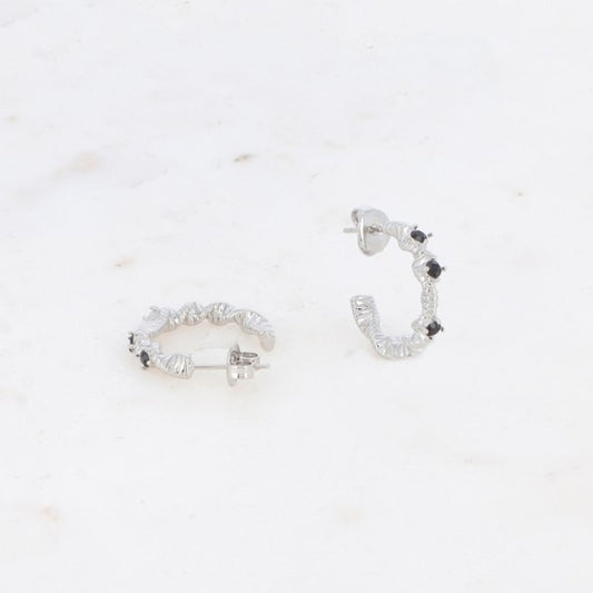 Et par små, sølvfarvede Fashion Paris-øreringe med snoet mønster og tre sorte sten på hver er vist på en hvid, let marmoreret baggrund - den ene ørering ligger fladt, mens den anden står oprejst.