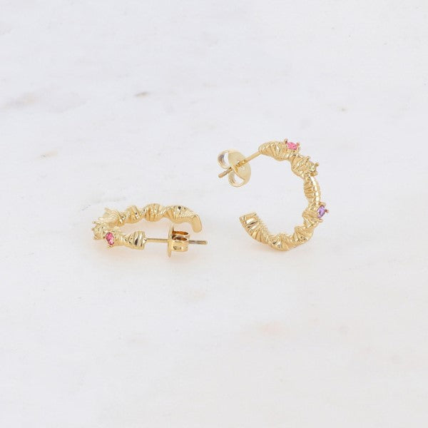 Et par Fashion Paris guld farve øreringe med et struktureret, krøllet design og små pink og lilla sten er udstillet på hvid marmor - den ene ørering står oprejst og viser stolpen, den anden ligger fladt.