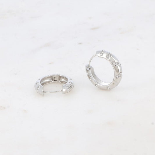 To små sølvøreringe fra Fashion Paris med hængslede spænder hviler på en hvid marmoroverflade. Hver ørering har jævnt fordelte, hævede blomstermotiver, og den glatte baggrund fremhæver deres delikate, elegante charme.