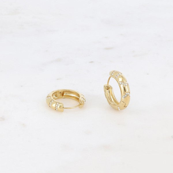 To små guldøreringe fra Fashion Paris med hængsellukning hviler på hvid marmor. Hver ørering har jævnt fordelte zirkonium-ædelstene, som giver det enkle gulddesign et glimt i øjet.