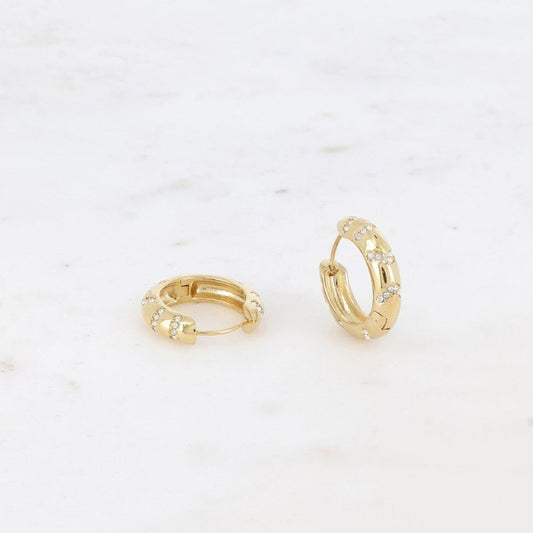 To små guldøreringe fra Fashion Paris med hængsellukning hviler på hvid marmor. Hver ørering har jævnt fordelte zirkonium-ædelstene, som giver det enkle gulddesign et glimt i øjet.