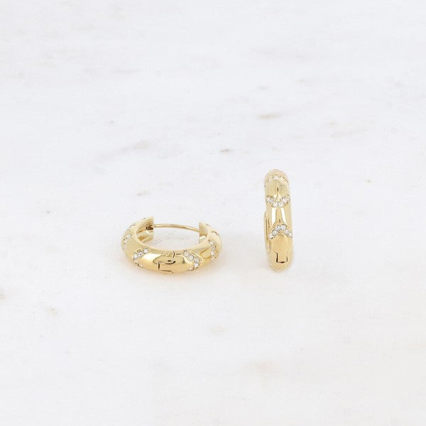 To små guldørestikker fra Fashion Paris med en glat, poleret finish hviler på hvid marmor. Hver ørering har klynger af funklende zirkoniumsten, som tilfører subtil glans og dekorative detaljer.