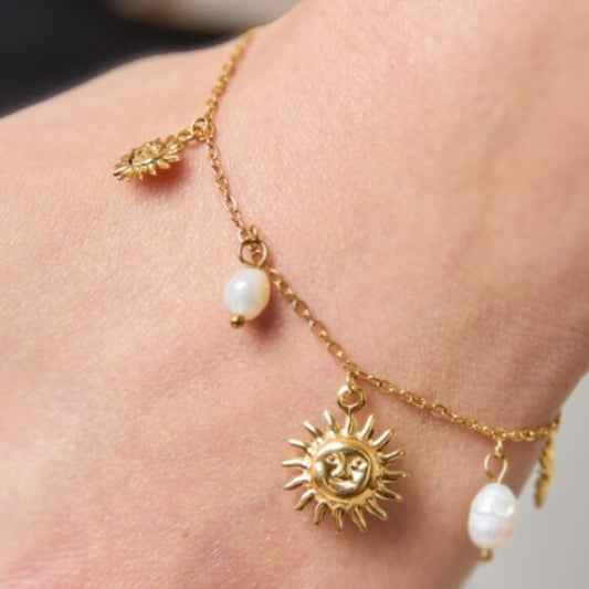 En guldfarvet ankelkæde fra Rouge Bonbons, fremstillet af rustfrit stål, har en detaljeret solansigtsvedhæng med mindre sol- og hvide perleaccenter, der giver et elegant look på anklen.