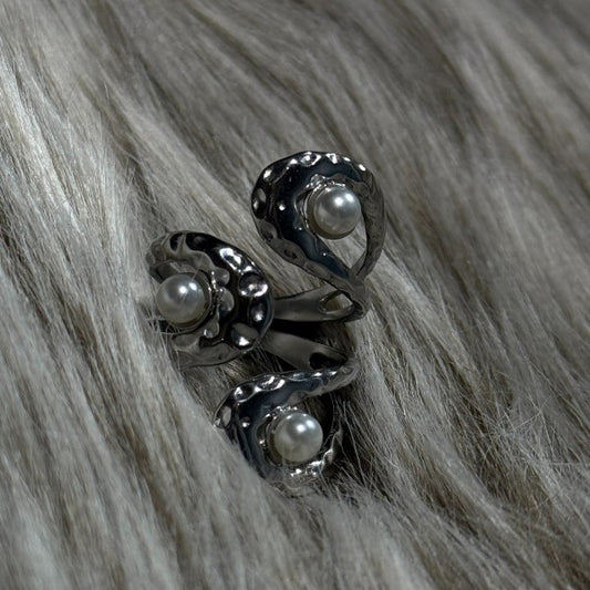 En sølvfarvede justerbar ring fra Rouge Bonbons har tre snoede bånd, der hver holder en rund hvid perle. Designet har små hævede prikker for tekstur og et marint udtryk, og ringen hviler på blødt gråt pels.