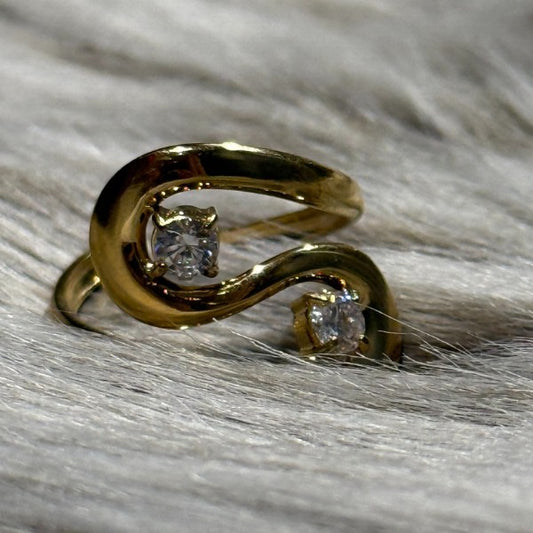 Rouge Bonbons-guldringen har et elegant hvirveldesign med to små runde diamanter i hver ende. Den polerede finish og de funklende sten, der er vist på blød lysegrå pels, skiller sig virkelig ud.