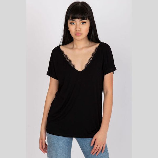 En ung kvinde med langt glat sort hår og pandehår er iført en løs Basic sort V-hals T-shirt med blondekant og lyseblå jeans. Hun står med ansigtet fremad mod en enkel, lys baggrund, der udtrykker tidløst design og komfort.