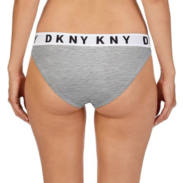 En person ses fra lænden og ned, iført en lysegrå DKNY Cozy Boyfriend trusse med en hvid elastisk linning med sorte DKNY-bogstaver. Den ensfarvede hvide baggrund fremhæver dette behagelige DKNY-undertøj.