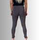 En person med langt, lysblondt hår bærer en sort top og tætsiddende leggings fra E Avantgarde, står barfodet og kigger væk mod en grå baggrund med armene langs siden.