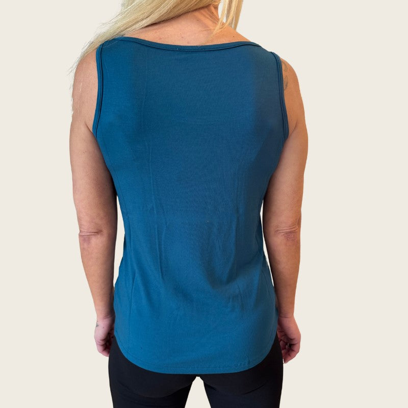 En kvinde med langt blondt hår ses bagfra iført en ærmeløs E Avantgarde OEKO-TEX-certificeret bambus-tanktop og sorte leggings. Den løstsiddende dametop har en lige kant og skiller sig ud fra den ensfarvede, lyse baggrund.