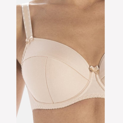 Et nærbillede viser en person iført en Teyli-bh i lys beige med tynde stropper, små dekorative sløjfer ved stroppernes basis og i midten, bøjlestøtte, subtile syningsdetaljer og afsløring af skuldre, øvre bryst og arm.