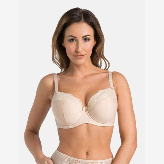 En kvinde med langt brunt hår står på en almindelig lys baggrund iført en beige-blond blonde-bh og matchende undertøj fra Teyli. Hun kigger fremad og ind i kameraet med et neutralt udtryk og den ene hånd hvilende på hoften.