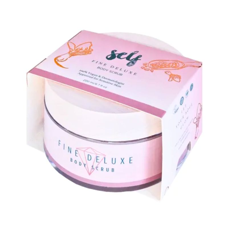 En lyserød og hvid krukke med Natural Self Fine Deluxe Body Scrub hviler delvist i sin matchende æske. Den elegante indpakning har guld-, rose- og blomsterdetaljer med tekst om dødehavssalt til glat, næret hud.