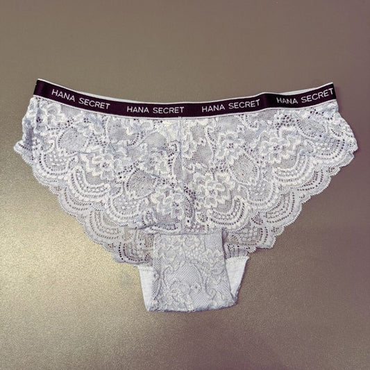 Et par lyse lavendelblå blondetrusser med et skulpteret blomsterdesign. På den sorte linning står der Jessylia i hvidt. Dette elegante lingeri er lagt fladt på en glat, neutral overflade.