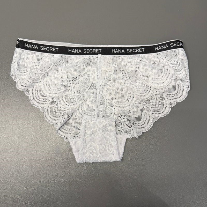 Et par hvide blondetrusser til kvinder fra Jessylia, stylet som White Brief, er lagt fladt på en grå overflade. Det har en sort linning med "HANA SECRET" i hvidt og delikate blomstermønstre med en skulpteret blondekant.