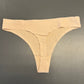 En JESSYLIA beige g-streng ligger fladt på en grå overflade og viser sit subtile diamantmønstrede stof og minimale design med en bred linning og smalle sektioner foran og bagpå.