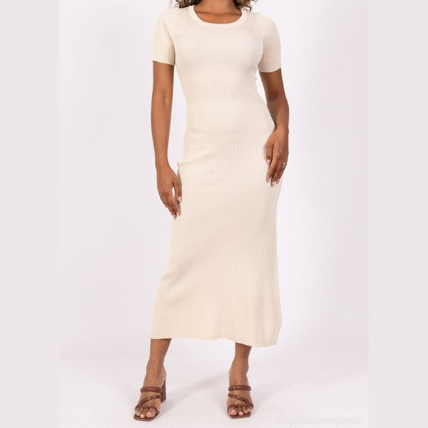 En kvinde viser en MOCHY lys beige, kortærmet ribstrik midi kjole med brune sandaler med hæl mod en hvid baggrund. Hendes hånd hviler på hoften, og hendes ansigt er ikke synligt i dette elegante outfit.
