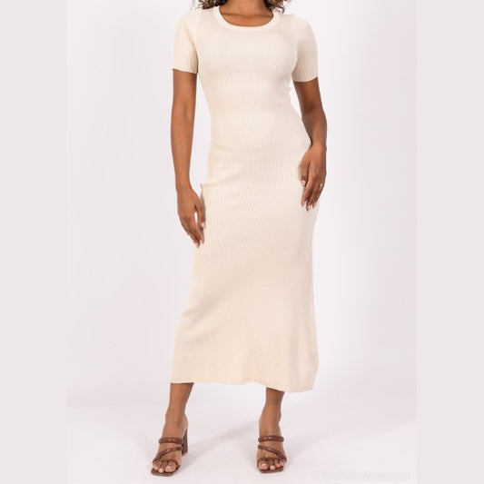 En kvinde viser en MOCHY lys beige, kortærmet ribstrik midi kjole med brune sandaler med hæl mod en hvid baggrund. Hendes hånd hviler på hoften, og hendes ansigt er ikke synligt i dette elegante outfit.