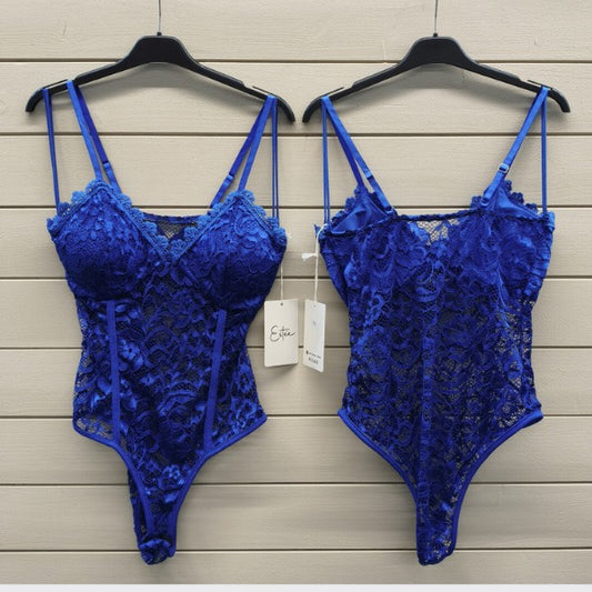To identiske ESTEE electric blue bodysuits hænger på sorte bøjler mod en lys trævæg. Disse lingeridele har tynde stropper, bøjlekopper, blomstrede blondedetaljer og et mærke på den ene.