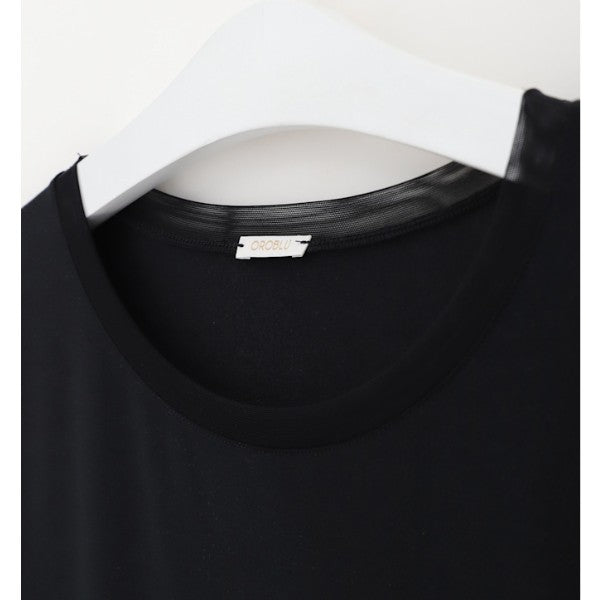 Et nærbillede af en sort Oroblu t-shirt med rund hals, der er ideel som en slags bluse, hænger på en hvid bøjle. T-shirten har en glat, almindelig tekstur med Oroblu-halsmærket synligt mod en enkel hvid baggrund.