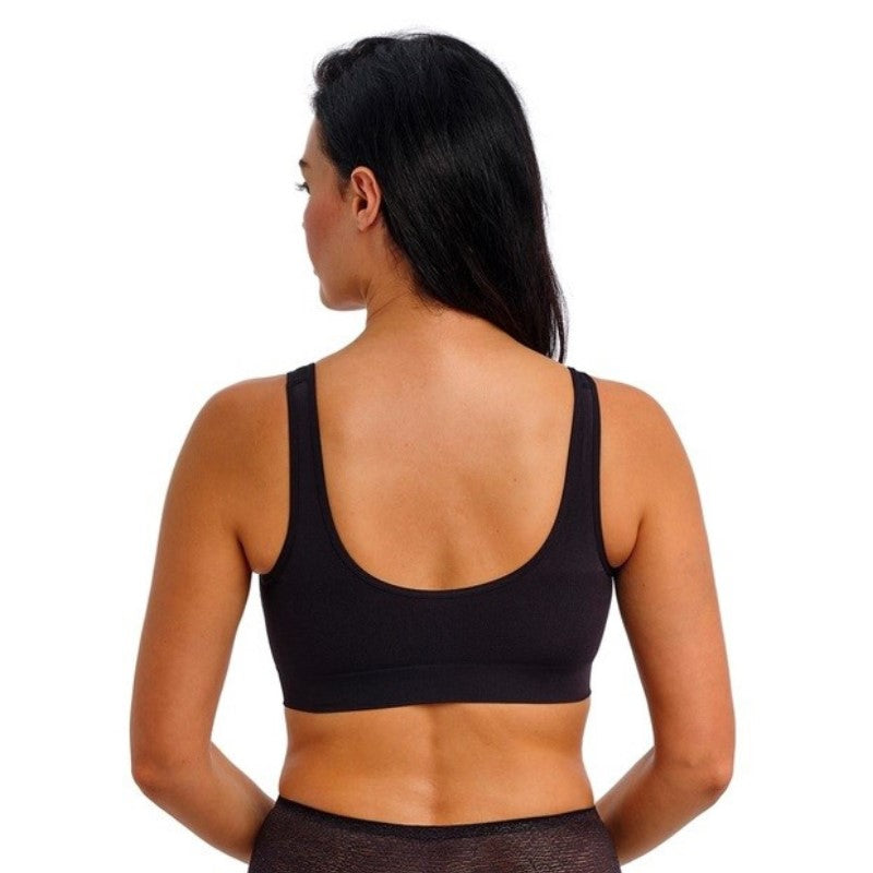 En kvinde med langt sort hår kigger væk fra kameraet og viser en Wacoal-bralette med brede stropper og rund ryg, parret med gennemsigtige sorte underbukser, mod en almindelig hvid baggrund.