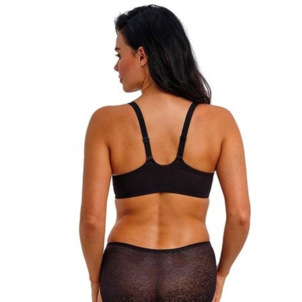 En kvinde med langt mørkt hår ses bagfra iført en sort Wacoal-bh med justerbare stropper og halvgennemsigtigt blondeundertøj, med armene afslappet i siden mod en almindelig hvid baggrund.